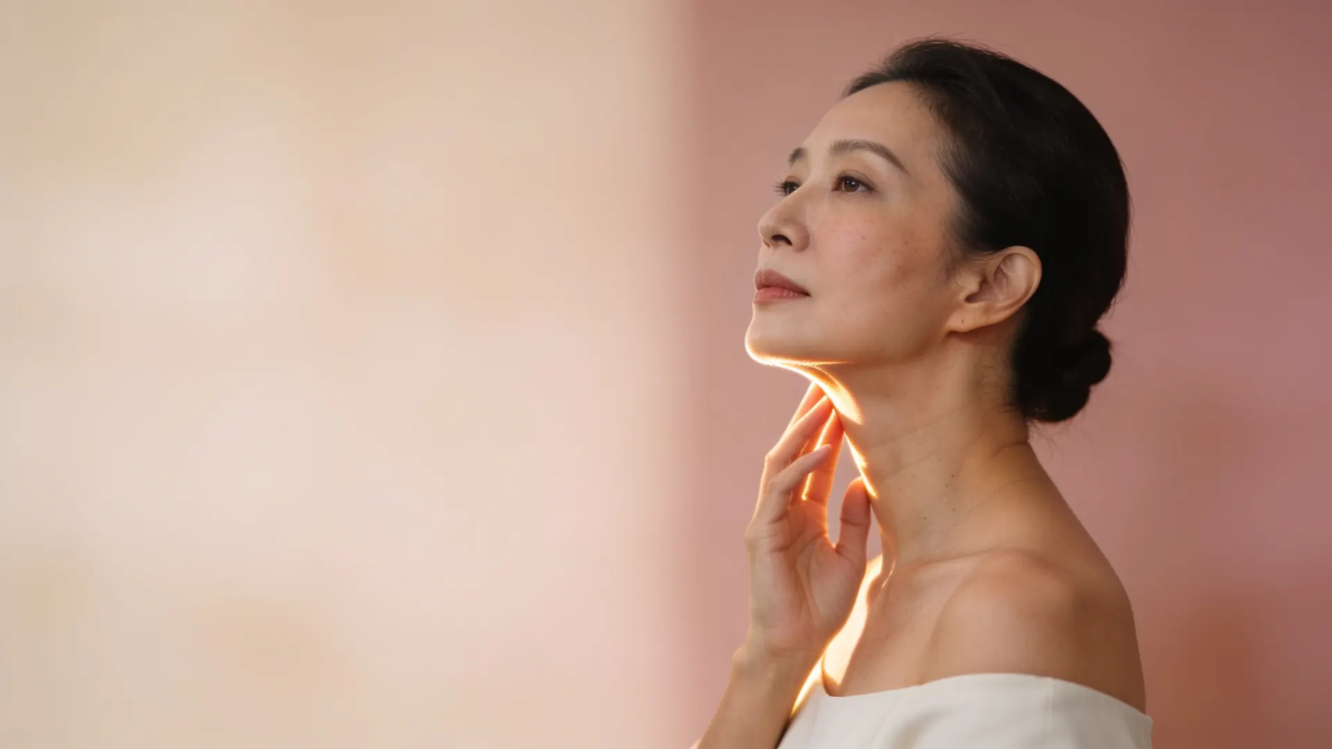 Illustrative image of a woman in profile with her hand beneath her chin, soft light along the jawline, against a blush pink wall